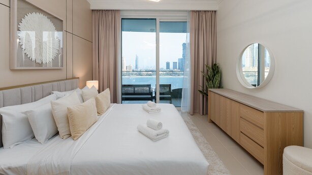 Ein modernes Hotelzimmer mit einem großen Bett, einer Holzkommode, einem runden Spiegel und Blick auf die Stadt durch das Fenster.