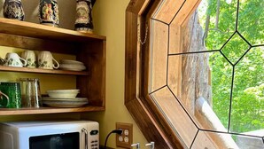 A kitchen with a white sink, a microwave, and a window with a hexagonal pattern.