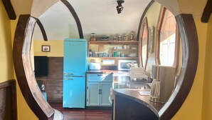 A kitchen with a blue refrigerator, wooden cabinets, and a window with curtains.