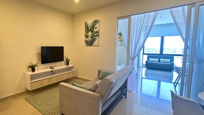 A modern living room with a sofa, a TV on a white console, a ceiling fan, and a large window with curtains.