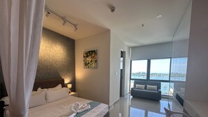 A modern hotel room with a large bed, a sitting area with a sofa, and a view of the sea through large windows.