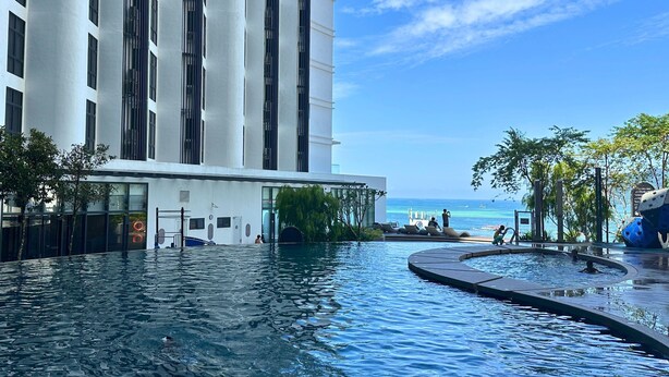 A modern hotel with a large pool area, a view of the ocean, and a clear sky.