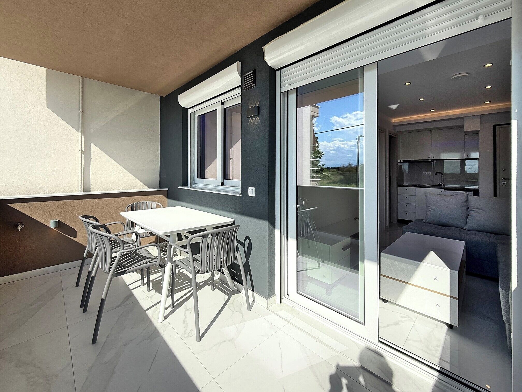 Un apartamento moderno con balcón, zona de comedor con mesa y sillas, y cocina visible a través de puertas de vidrio.