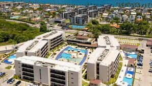 An aerial view of a coastal hotel complex with multiple buildings, a central swimming pool, and a parking area. - Refuge By Paty - Malia Beach Resort for families (Ipojuca)