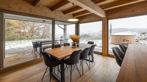Ein Essbereich aus Holz mit einem großen Tisch und Stühlen, große Fenster mit Blick auf eine verschneite Landschaft und einem Whirlpool im Freien.