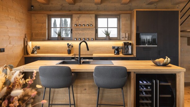 Eine moderne Küche mit Holzwänden, einer zentralen Kochinsel mit zwei Barhocker, einer Spüle und einem integrierten Weinkühlschrank.