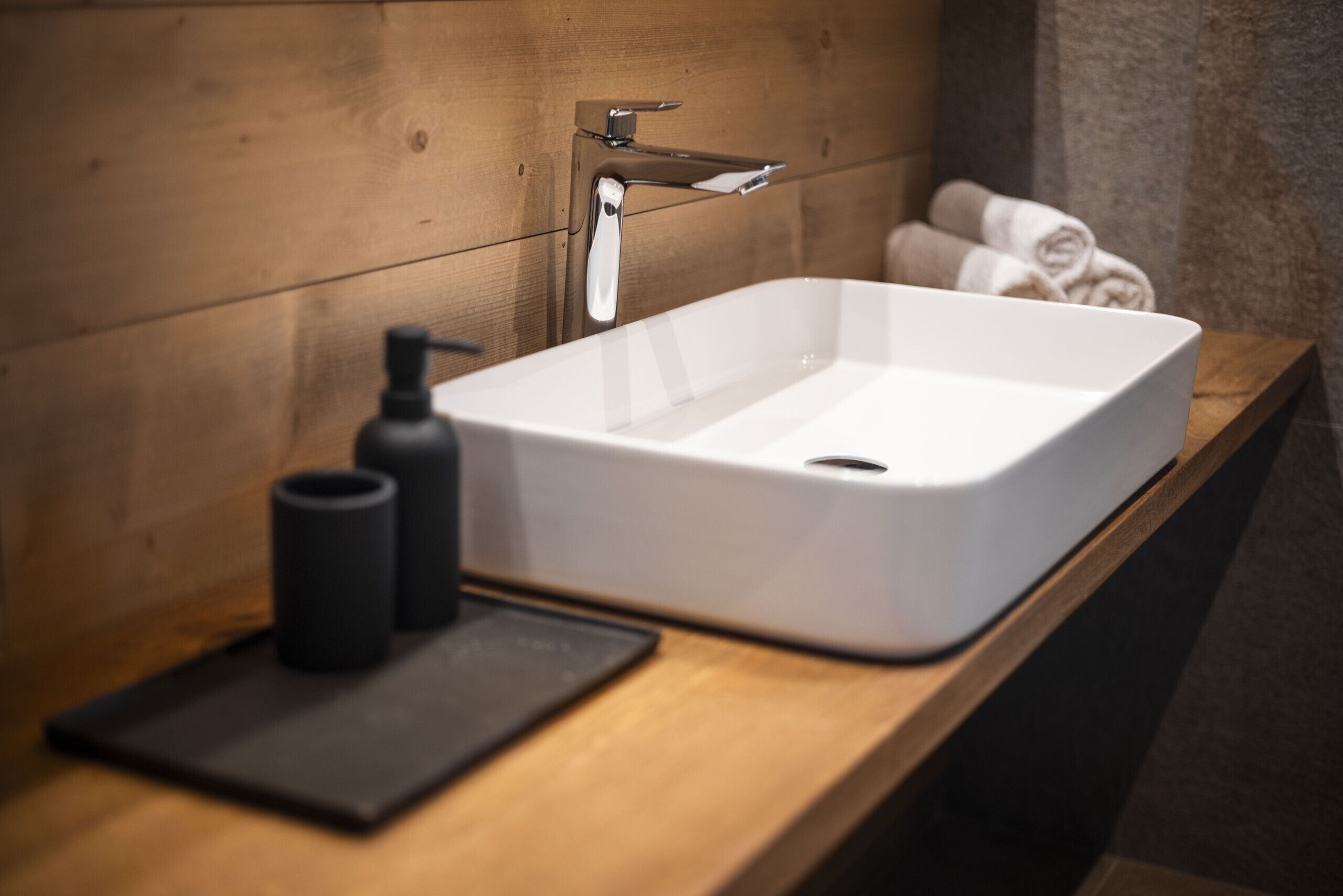A bathroom with a white sink, a wooden countertop, and a towel rack with towels.