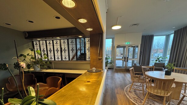 A hotel lobby with a wooden reception desk, seating area, and potted plants. - Motellet Karlskrona (Karlskrona)