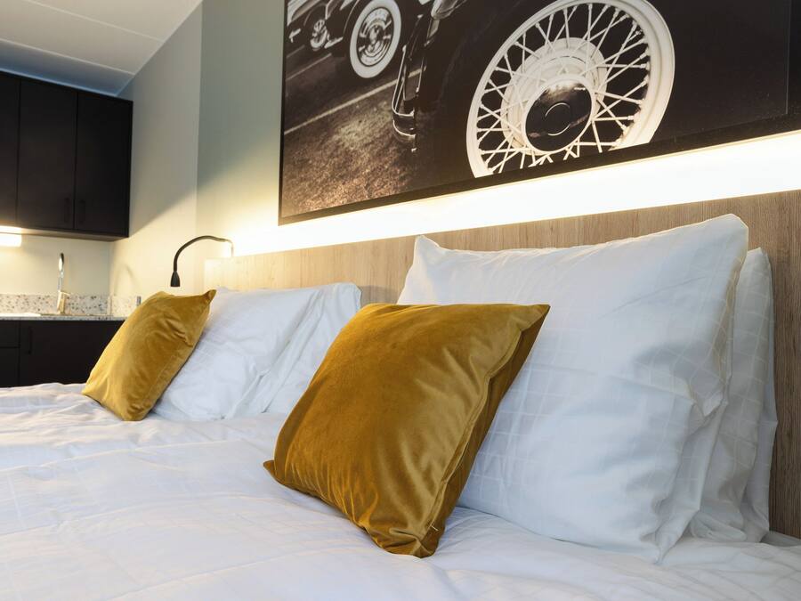 A hotel room with a bed, white bedding, a headboard, and a wall-mounted artwork.