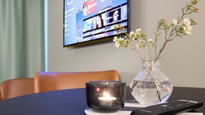 A modern room with a TV displaying streaming services, a candle on a table, and a vase with flowers. - Motellet Karlskrona (Karlskrona)