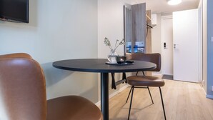 A modern dining area with a round table, two brown leather chairs, a vase with flowers, and a flat-screen TV mounted on the wall. - Motellet Karlskrona (Karlskrona)