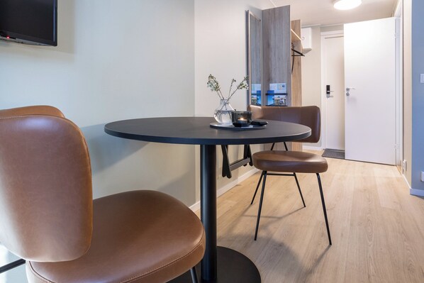 A modern dining area with a round table, two brown leather chairs, a vase with flowers, and a flat-screen TV mounted on the wall. - Motellet Karlskrona (Karlskrona)