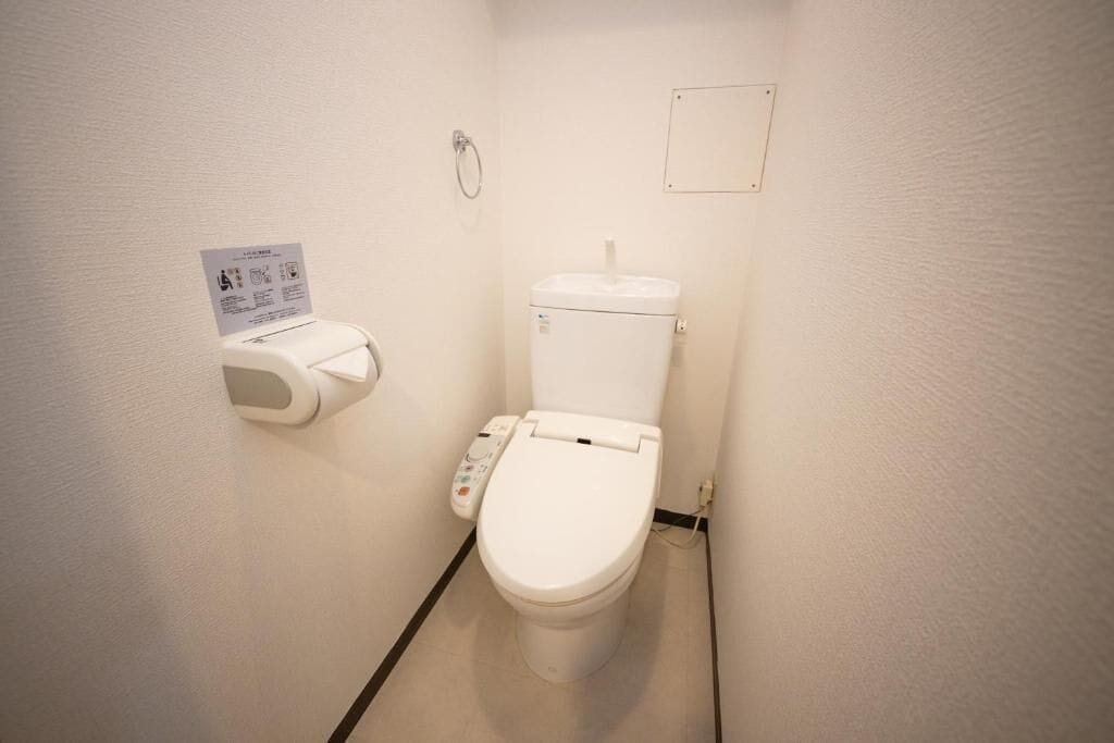 Pieni, valkoinen kylpyhuone, jossa on wc, paperipyyhkeiden annostelija ja käsidesiannostelija.