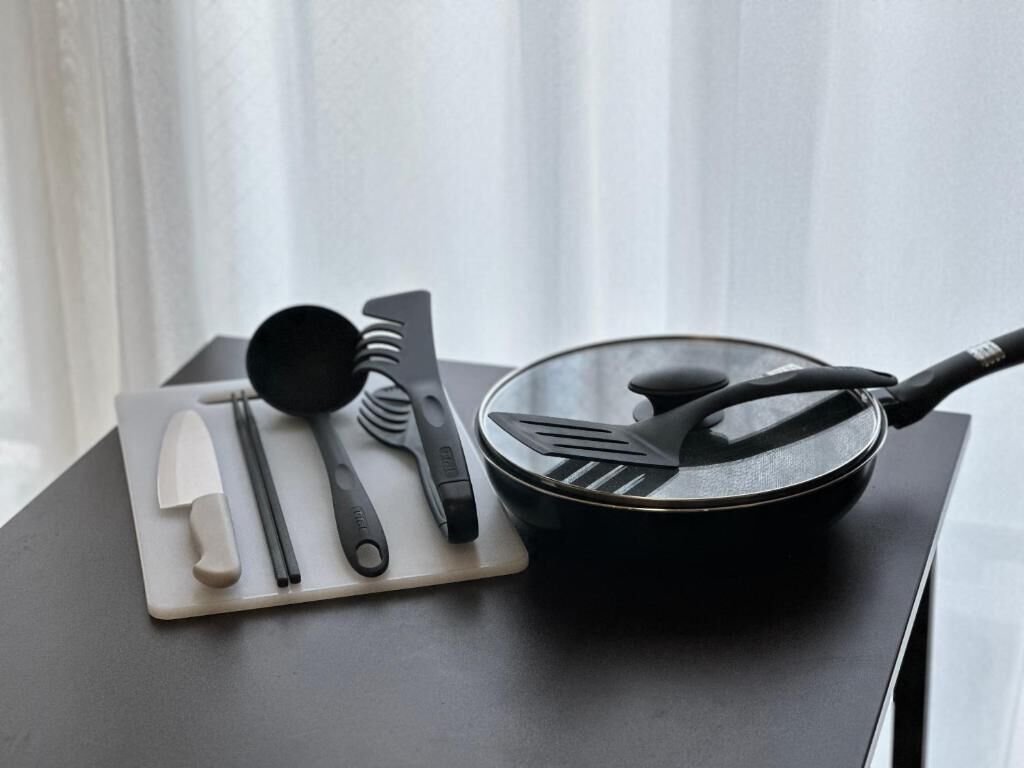 A kitchen counter with a frying pan, spatula, and chopsticks on a cutting board.
