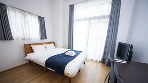Ein Hotelzimmer mit einem Bett, einem Schreibtisch mit Computer und großen Fenstern mit Vorhängen.