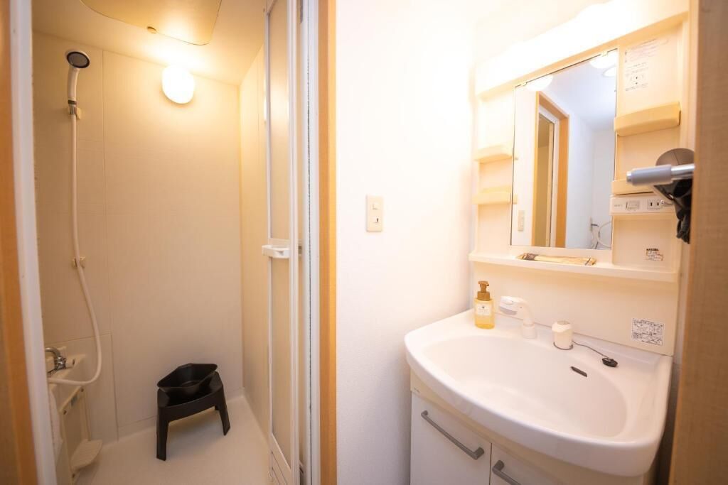 A bathroom with a shower, a sink, a mirror, and a small stool.