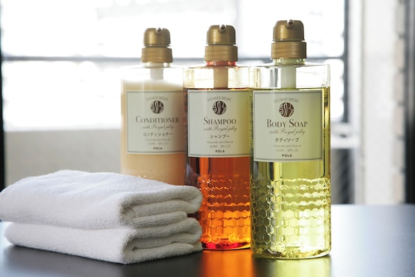 Trois bouteilles de produits de douche sont posées sur une table, à côté d’une serviette blanche pliée.