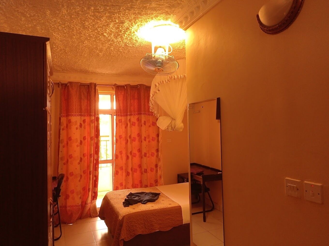 A small, cozy room with a single bed, a chair, a desk, and a mirror.
