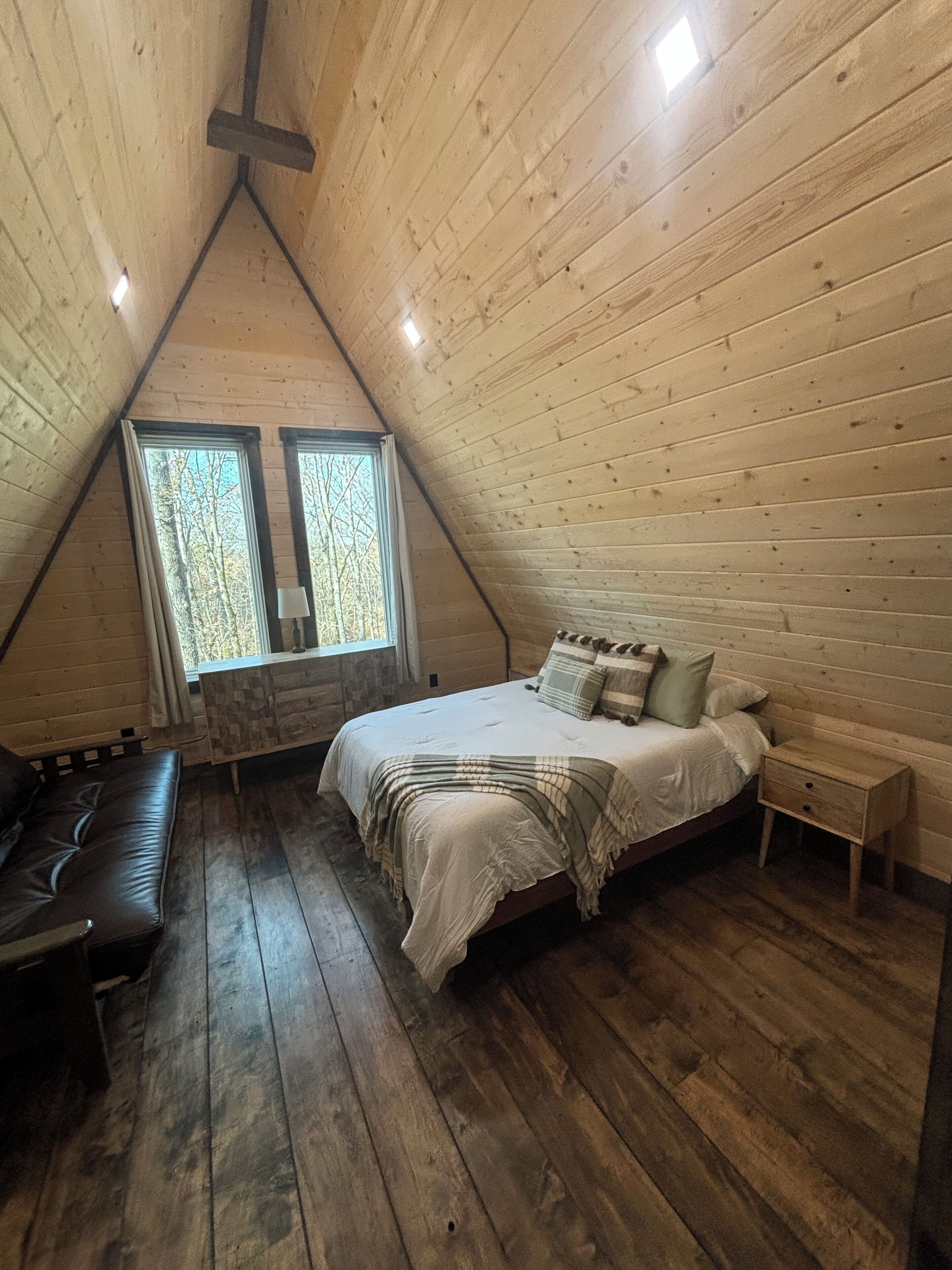 A cozy, triangular wooden room with a bed, a bench, and a nightstand.