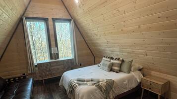 A cozy, triangular wooden room with a bed, a bench, and a nightstand.