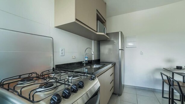 A compact kitchen with a gas stove, stainless steel refrigerator, and a small dining area. - Apt in Condo w/ Pool and Gym Rgk1202 (Poços de Caldas)