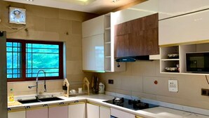 A modern kitchen with white cabinets, a built-in oven, and a window with a view of greenery. - Sujimoto Residences - The AVEs  (Lagos)