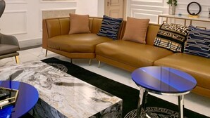 A modern living room with a sectional sofa, a marble coffee table, a blue side table, and a decorative floor rug. - Sujimoto Residences - The AVEs  (Lagos)