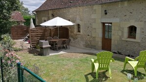 Een stenen gebouw met een patio, compleet met een tafel, stoelen, een houten schutting en een groene stoel.