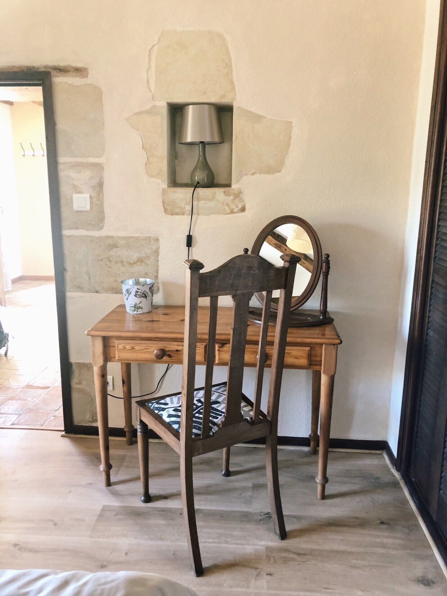 A wooden dining table with a chair, a wall-mounted lamp, and a vase on a stone wall.