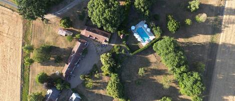 Eine Luftaufnahme eines Anwesens mit Swimmingpool, einem großen Gebäude mit mehreren Zimmern und umgebender Grünfläche.