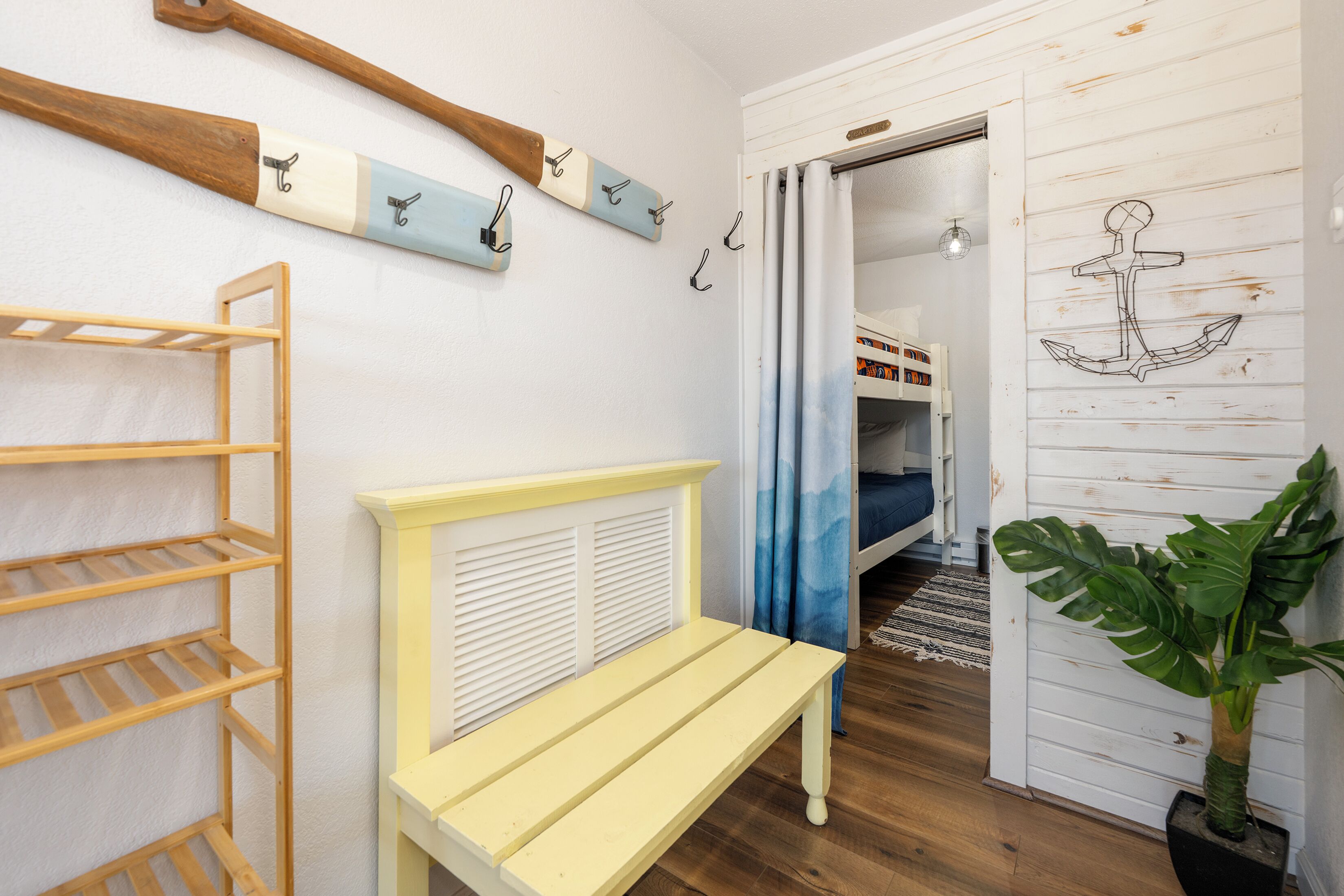 Una habitación con un banco de madera, un perchero en la pared, una cama con cortina azul y una planta en maceta.