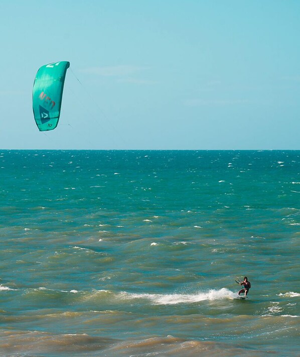Una persona practica windsurf en el océano con una cometa verde.