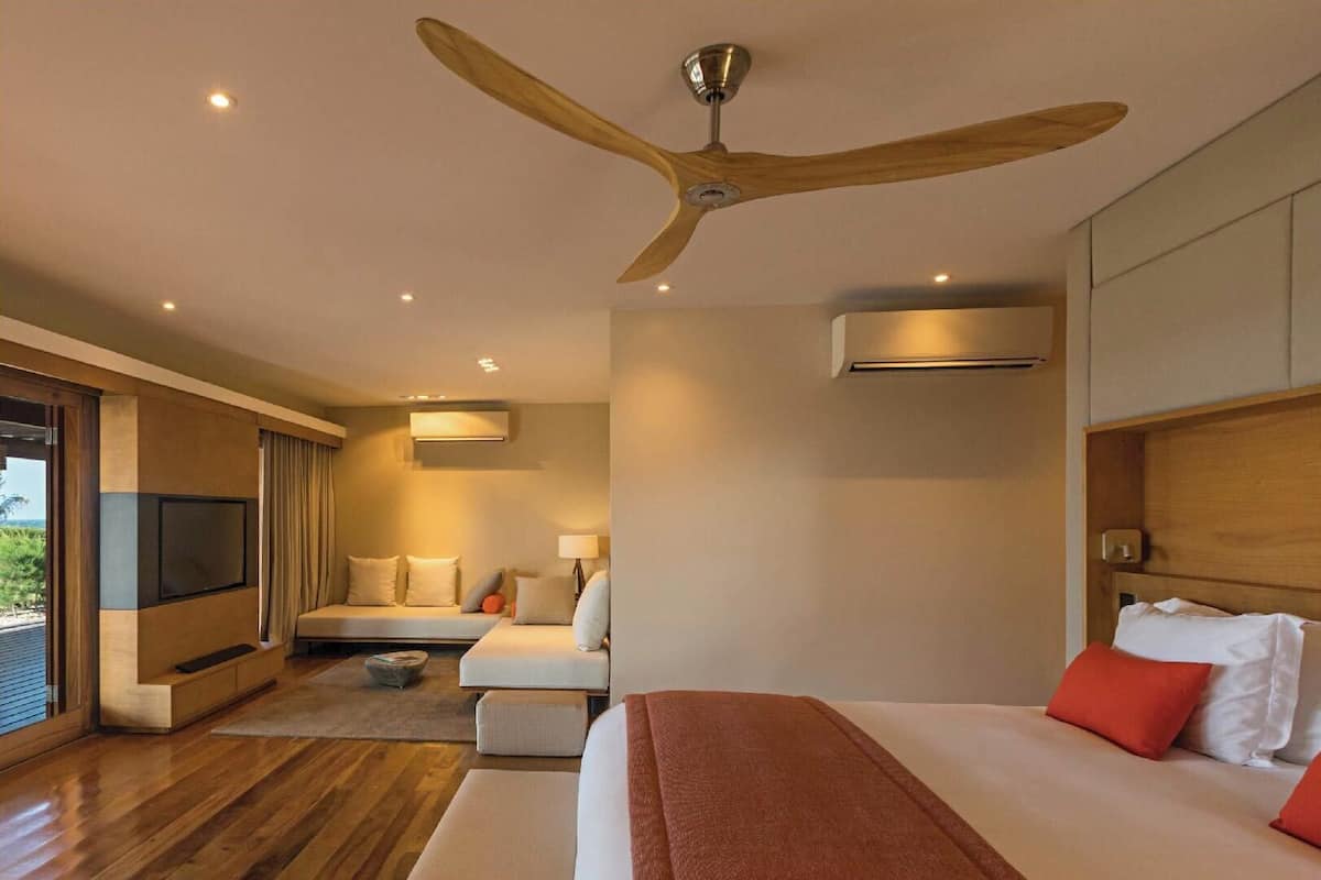 A modern hotel room with a large bed, a ceiling fan, a TV, and a balcony with a view.