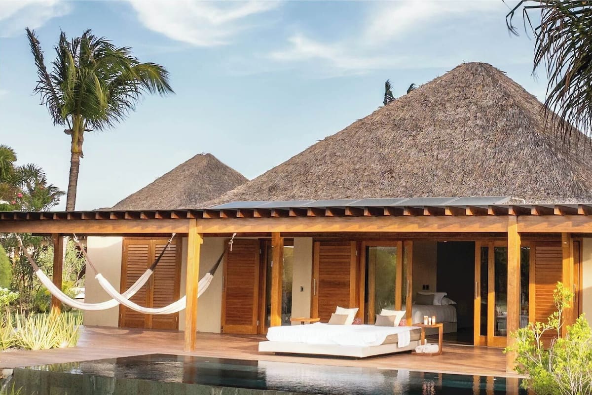 A modern resort with a pool, wooden deck, and thatched-roof structures.