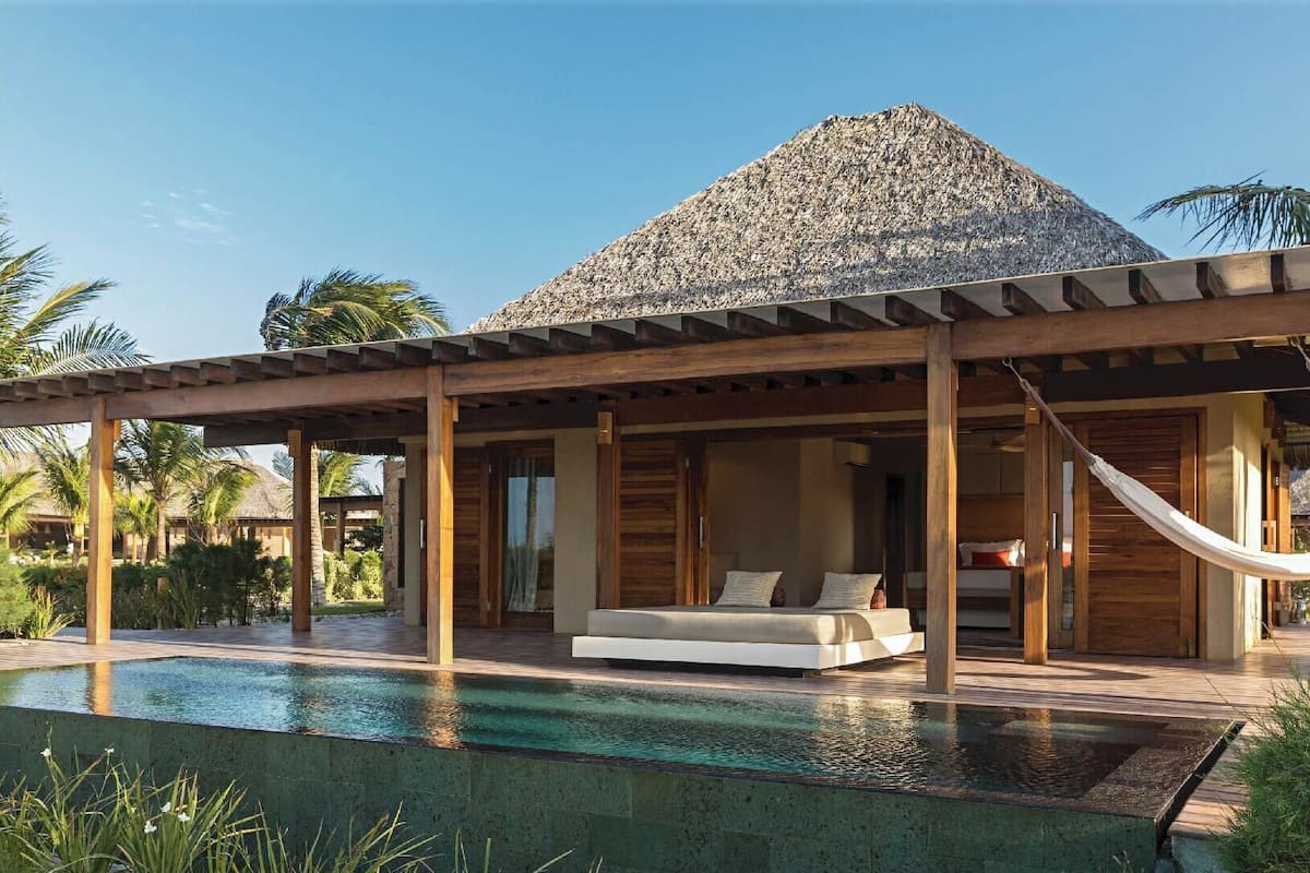 A modern resort with a pool, wooden deck, and a thatched-roof structure.