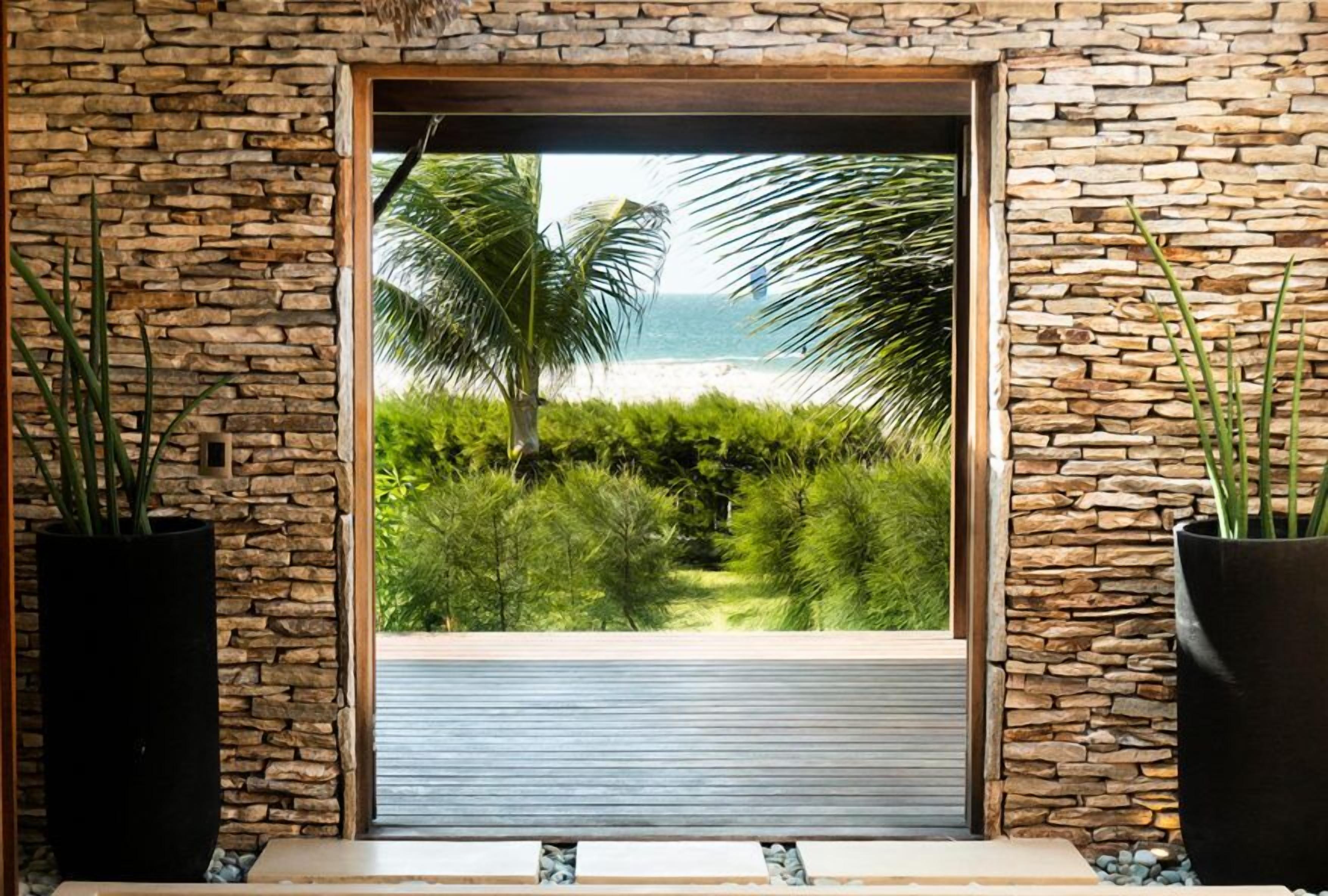 A view through a stone-framed window with a palm tree and ocean in the background.