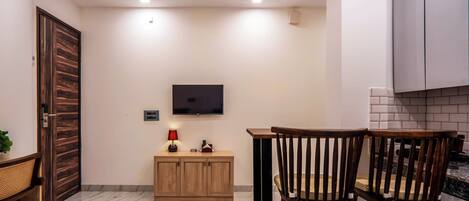 Una cocina moderna con un televisor montado en la pared, armarios de madera, suelo de mármol y un comedor con dos sillas de madera.