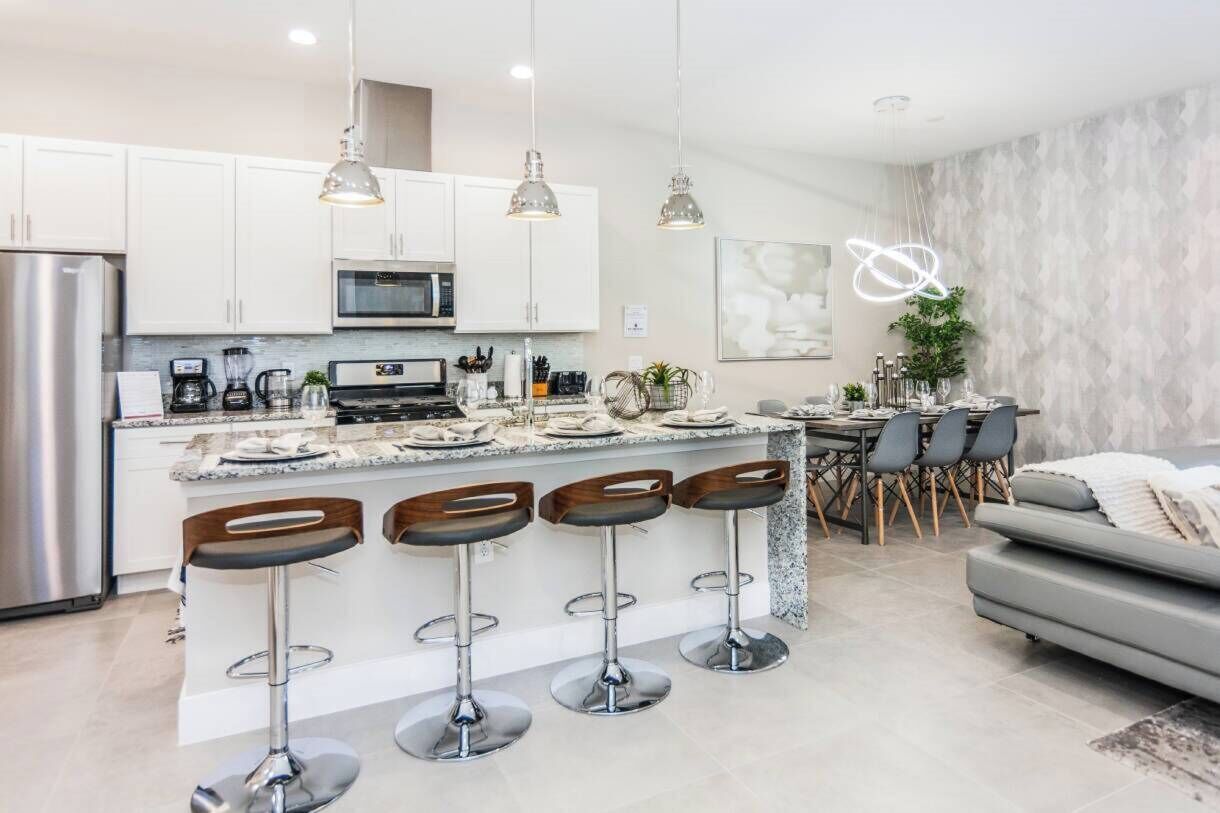 A modern kitchen with white cabinets, a central island with bar stools, stainless steel appliances, and pendant lighting.