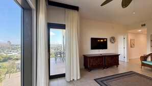 Ein geräumiges Wohnzimmer mit einer großen Schiebeglaswand, die auf einen Balkon führt, einem an der Wand montierten Flachbildfernseher und einem Holzschrank.