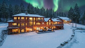 En stor, fleretages hytte med et snedækket landskab og udsigt til nordlys.