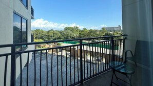 A balcony with a view of a parking lot and greenery, a chair, and a building in the background. - Cozy Studio w/ a short walk to Beach & Free round of Golf & Activities Daily! (Panama City Beach)