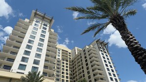 A high-rise building with multiple balconies and a palm tree in the foreground. - Cozy Studio w/ a short walk to Beach & Free round of Golf & Activities Daily! (Panama City Beach)