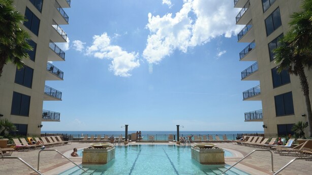 A pool area with clear blue water, lounge chairs, and a view of the ocean. - Cozy Studio w/ a short walk to Beach & Free round of Golf & Activities Daily! (Panama City Beach)
