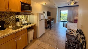 A compact kitchen with wooden cabinets, a microwave, and a refrigerator. There is a dining area with a table and chairs, and a balcony with a view. - Cozy Studio w/ a short walk to Beach & Free round of Golf & Activities Daily! (Panama City Beach)