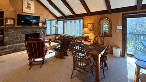 A cozy living room with a stone fireplace, wooden furniture, and a television mounted on the wall. - Spacious Sugar Mountain Condo with Golf Course Views & Prime Location (Sugar Mountain)