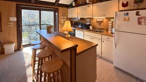 A kitchen with a wooden island, bar stools, a refrigerator, and a view through a glass door to an outdoor deck. - Spacious Sugar Mountain Condo with Golf Course Views & Prime Location (Sugar Mountain)