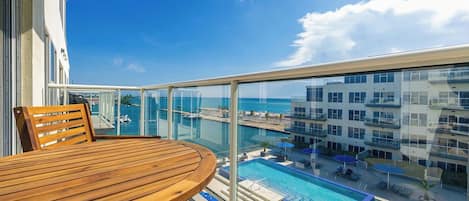 A balcony with a wooden table and chairs, overlooking a swimming pool and a marina.