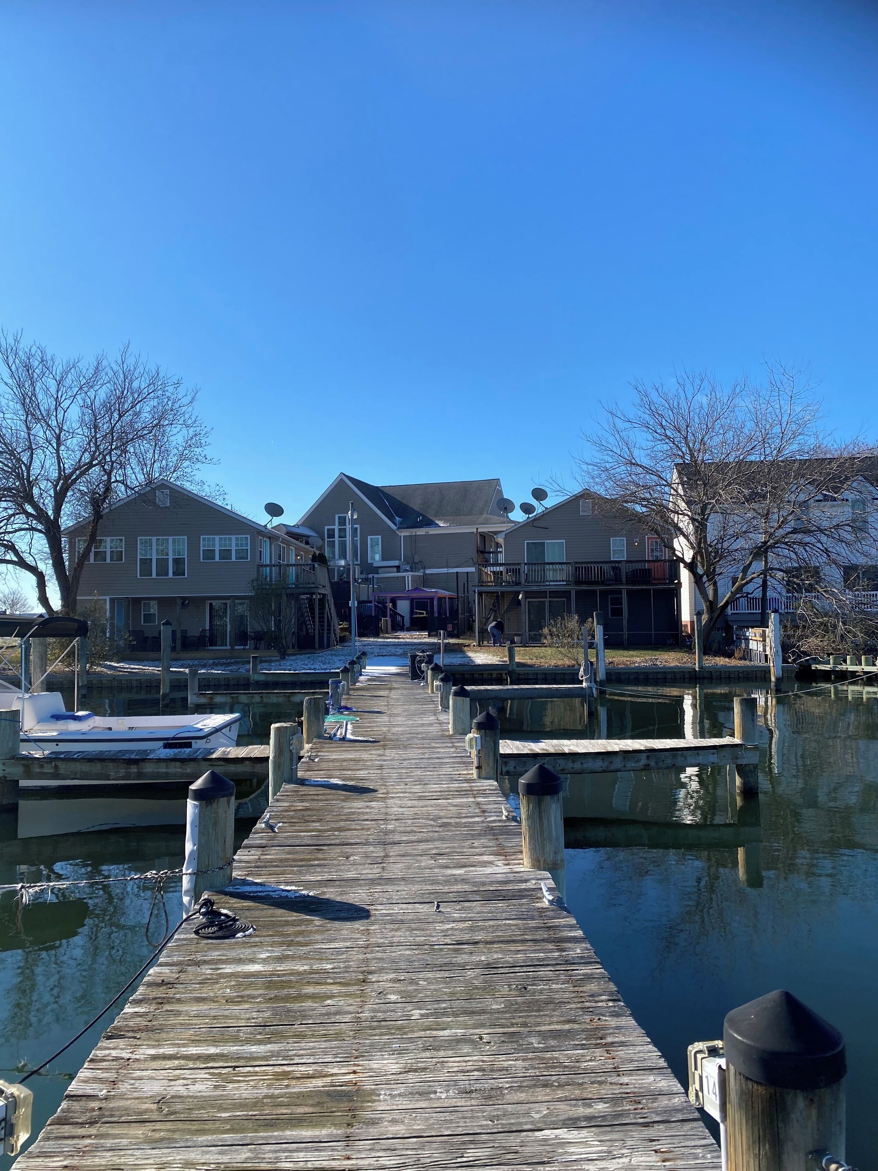 A wooden pier leading to a marina with houses in the background.