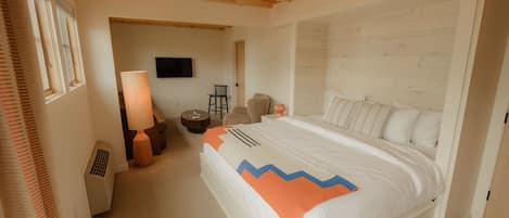 Een slaapkamer met een houten plafond, een bed met een gestreept kussen, een stoel, een lamp en een televisie aan de muur.