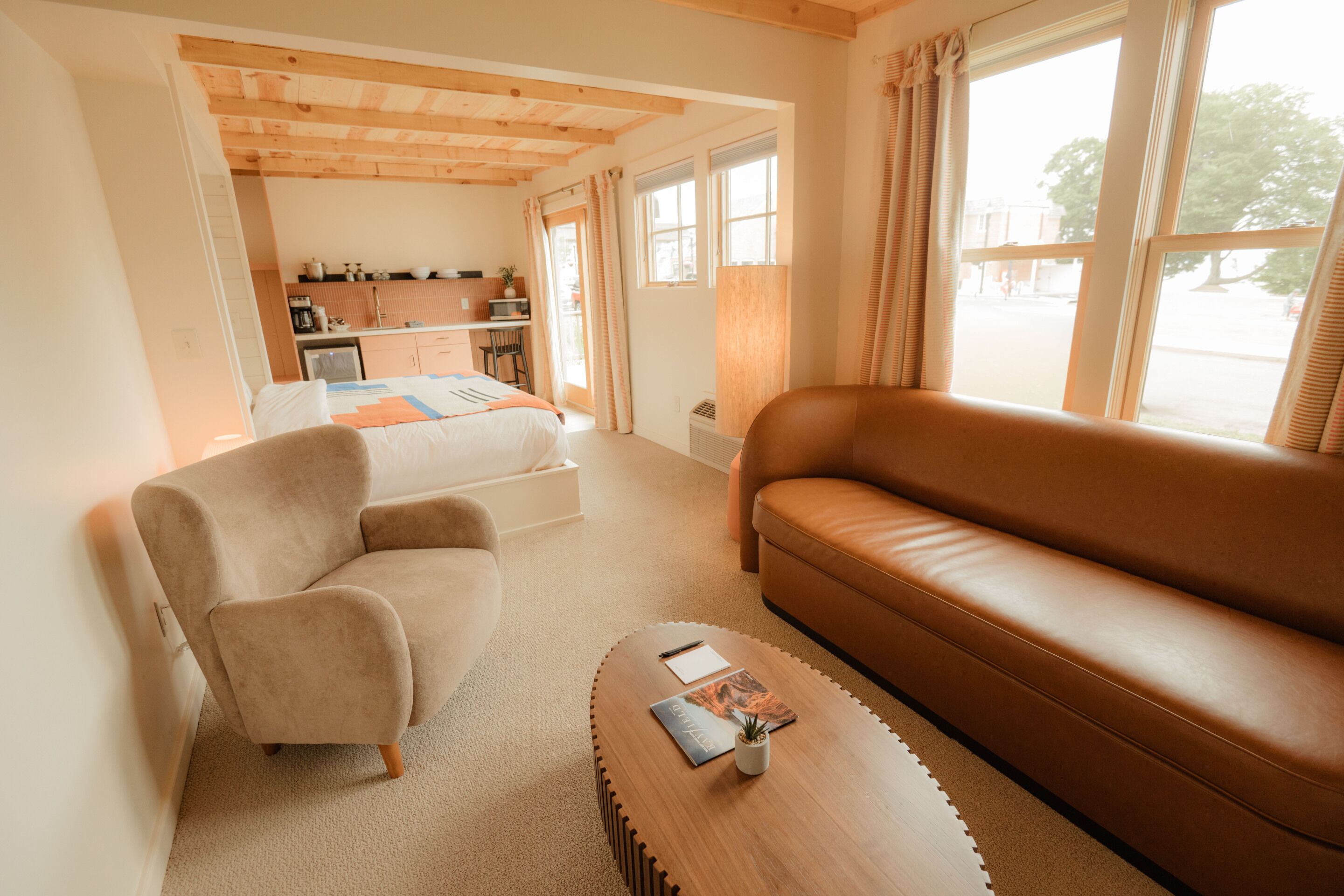 A room with a bed, a sofa, a coffee table, and a kitchenette in the background.